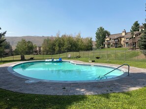 Ein Schwimmbecken mit gepflastertem Deck, umzäunt und mit Blick auf Wohnhäuser im Hintergrund.