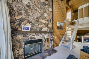 Ein Steinkamin mit Holzvorrat, eine Holztreppe und ein rustikales Interieur.