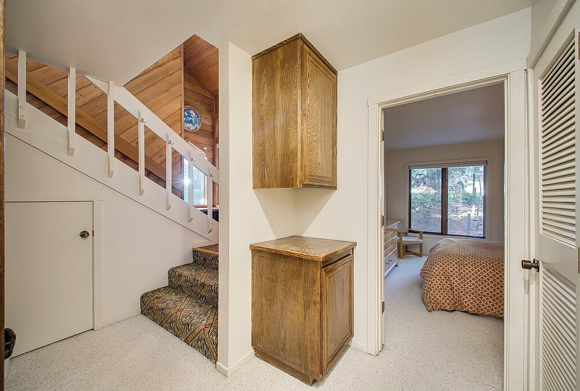 Un escalier avec des finitions en bois, une petite armoire en bois et une chambre à coucher avec un lit et une fenêtre.