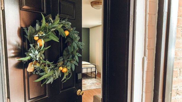 A dark wooden door with a wreath of green leaves and oranges, leading to a room with a bed and a white wall. - Steps to VT Campus & Cassell Cozy Blacksburg Studio (Blacksburg)