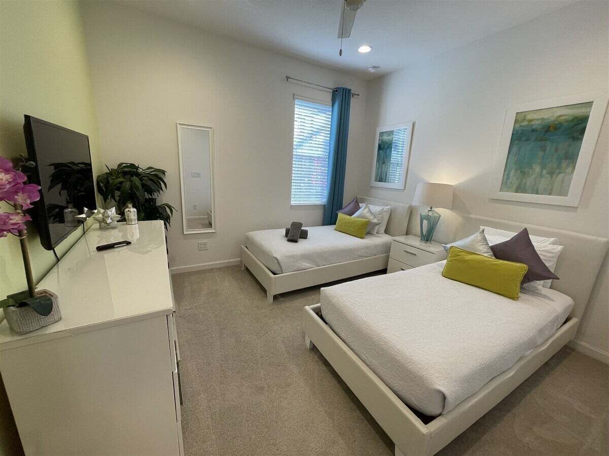 A modern bedroom with two beds, a desk, a mirror, and a window with curtains.