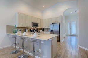 A modern kitchen with white cabinets, stainless steel appliances, and a bar area with stools.