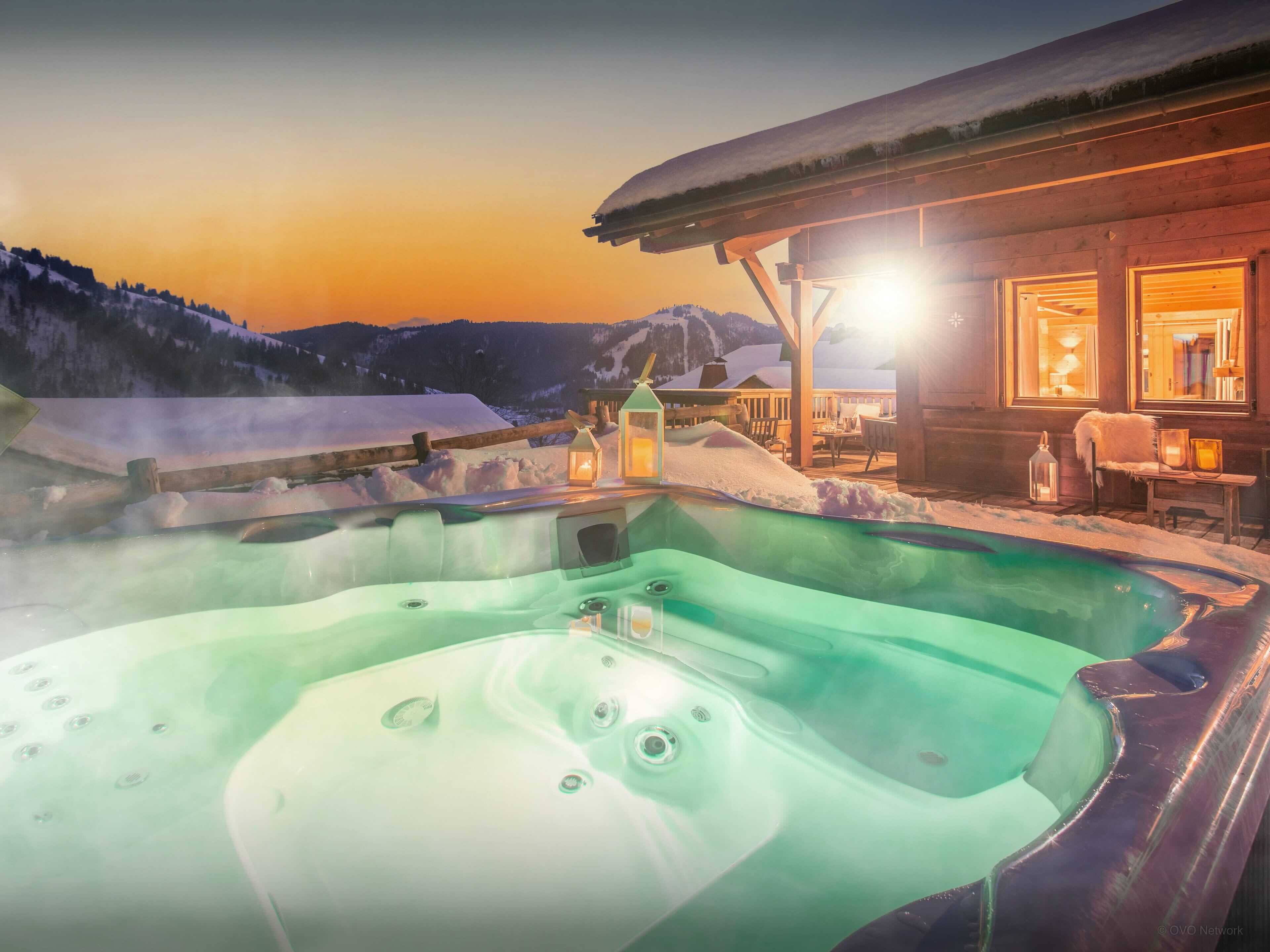 A hot tub with a wooden deck and a wooden cabin in the background.