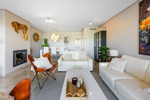 A modern living room with a fireplace, white sofas, a dining area, and decorative wall art.