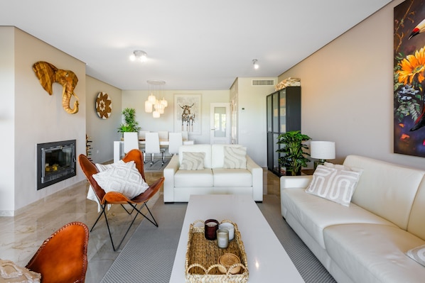 A modern living room with a fireplace, white sofas, a dining area, and decorative wall art.