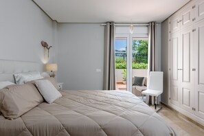 A bedroom with a large bed, a chair, a nightstand, and a view of the outdoors.