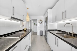 A modern kitchen with white cabinets, black countertops, stainless steel appliances, and a hanging pendant light.