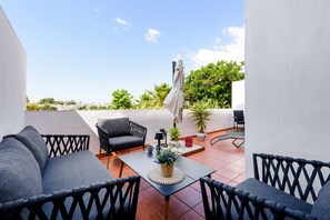 A rooftop terrace with a sofa, chairs, a table, and a potted plant.