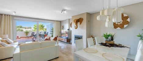 A modern living room with a sofa, dining table, and chairs. There is a large window with a view of the outdoors.