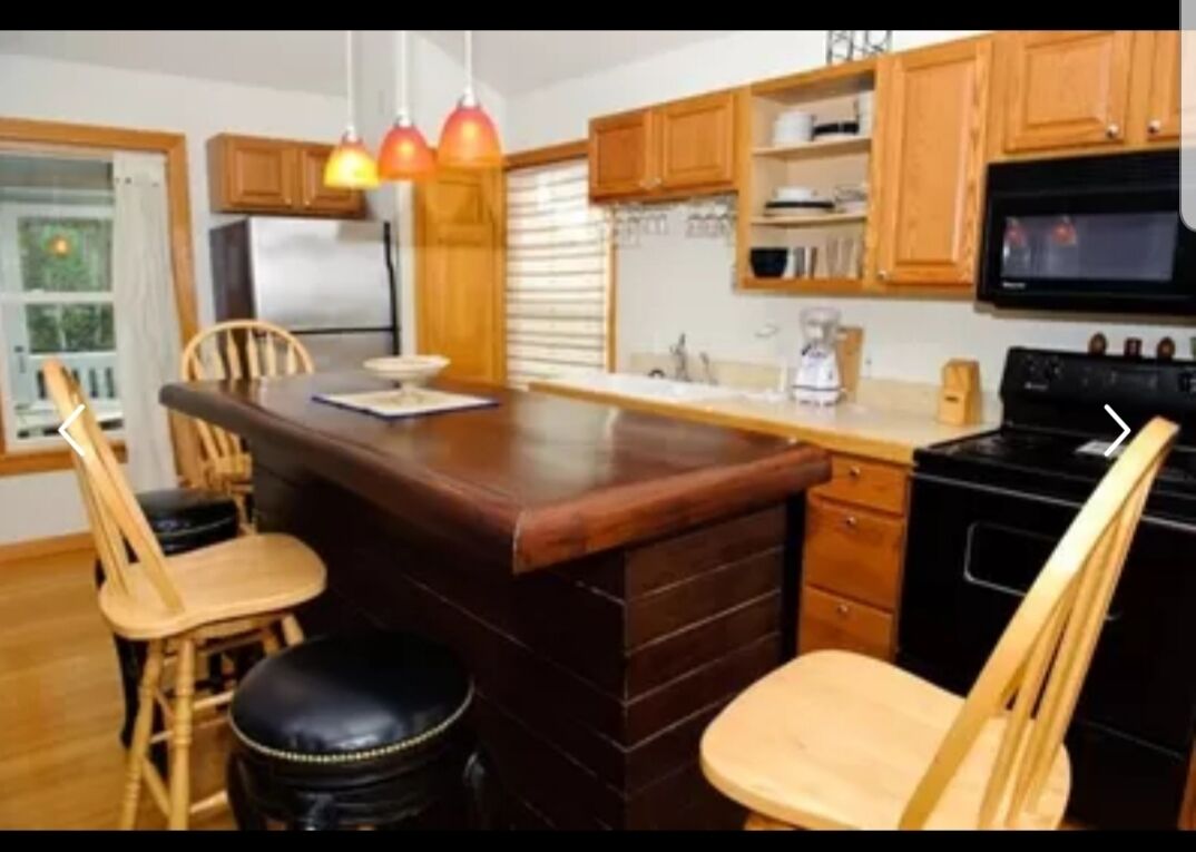 Une cuisine avec des meubles de rangement en bois, un îlot central doté de tabourets, un réfrigérateur et une cuisinière.