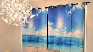 Ein Essbereich mit einem Holztisch und Stühlen, einer dekorativen Chandelier und Vorhängen mit einer Strandansicht.