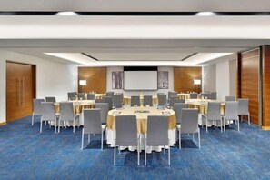 A conference room with round tables, chairs, a projector screen, and a carpeted floor. - Fairfield by Marriott Bengaluru Whitefield (Bengaluru)