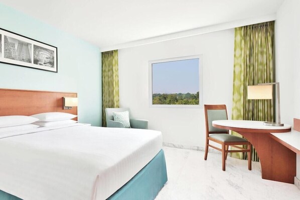 A hotel room with a bed, a desk, a chair, a window with a view, and a wall-mounted picture. - Fairfield by Marriott Bengaluru Whitefield (Bengaluru)
