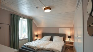 A bedroom with a bed, two bedside tables, a window with curtains, a ceiling light, and a wall-mounted mirror. - 3 bedroom beautiful home in Ambjörby (Ambjörby)