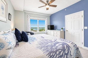 A bedroom with a bed, a TV on a dresser, a ceiling fan, and a window with a view.