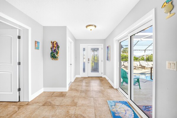 A hallway with a tiled floor, white walls, and a glass door leading to a pool area. - Across From Beach | Private Pool | Hope's Haven (Port Orange)