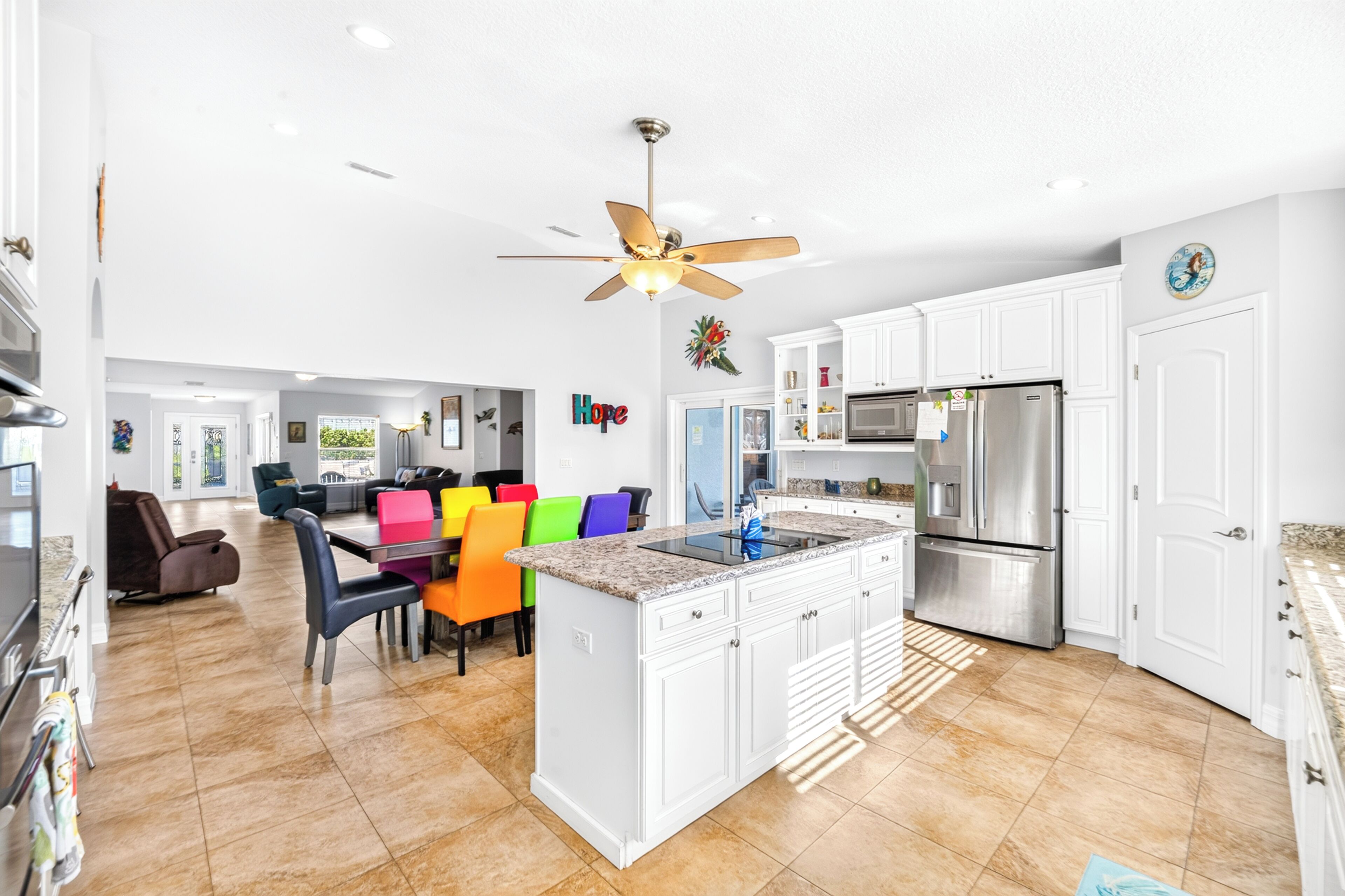 A spacious kitchen with white cabinets, a stainless steel refrigerator, and a dining area with colorful chairs.