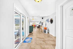 Ein Korridor mit einer Glastür, die zu einem Poolbereich führt, einem Deckenventilator und einem Essbereich in der Ferne.
