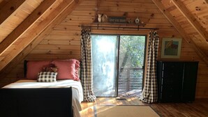 Une chambre mansardée chaleureuse, avec un lit, des rideaux à carreaux, un plafond en bois, une fenêtre et une pancarte sur laquelle on peut lire : « Je t’aime plus que tout ».