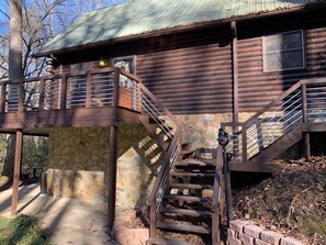 Une cabane en rondins avec des fondations en pierre, un balcon doté d’une rambarde en métal et un escalier menant à l’entrée principale.