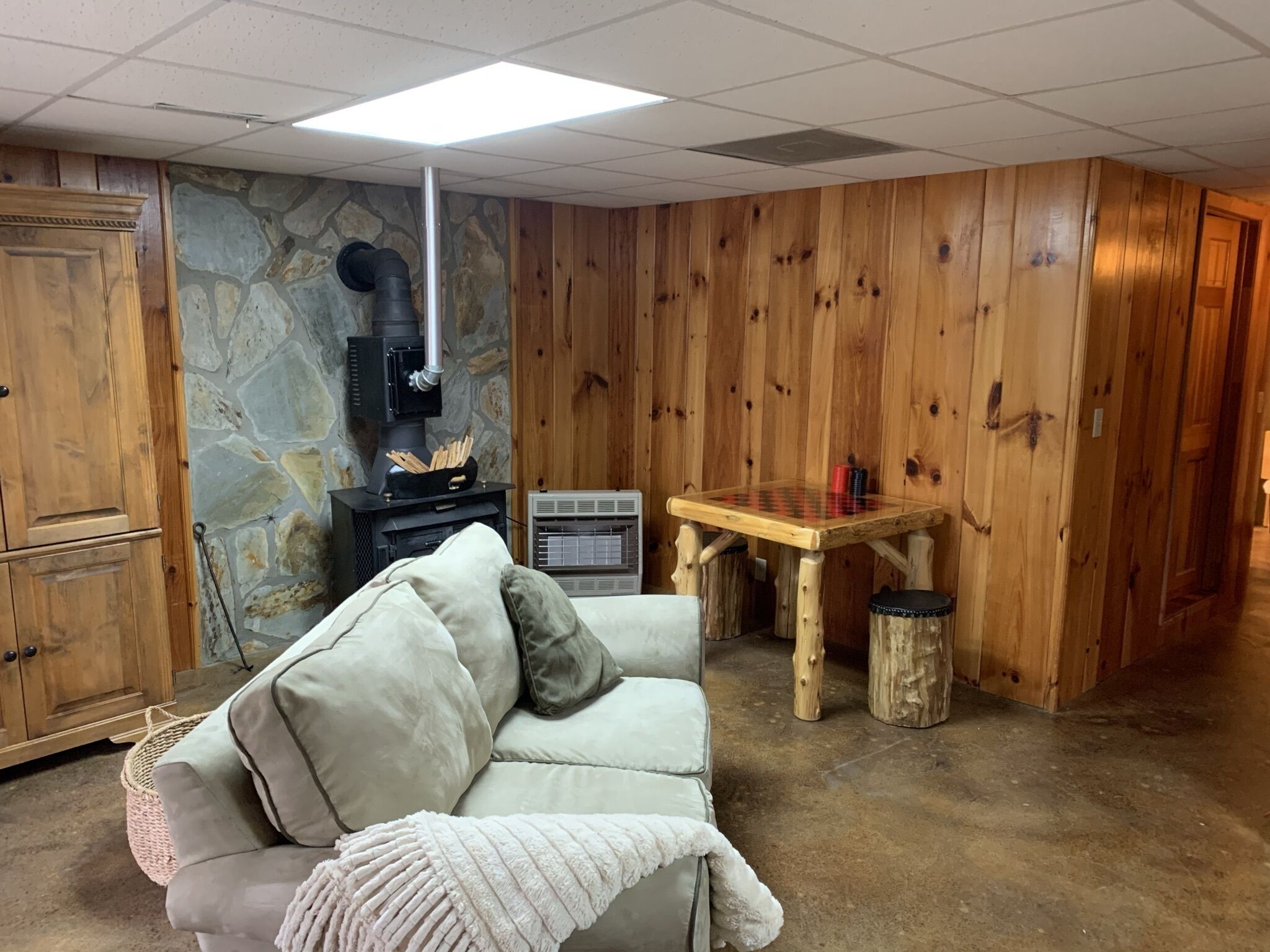 A cozy room with a stone wall, wooden paneling, a fireplace, a sofa, and a small wooden table.