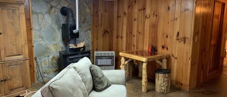 A cozy room with a stone wall, wooden paneling, a fireplace, a sofa, and a small wooden table.