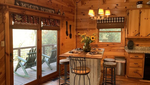 L’intérieur d’un chalet en bois comprend un coin repas, des tabourets de bar, une cuisine dotée de plans de travail en granit et une vue sur l’extérieur à travers les portes vitrées.