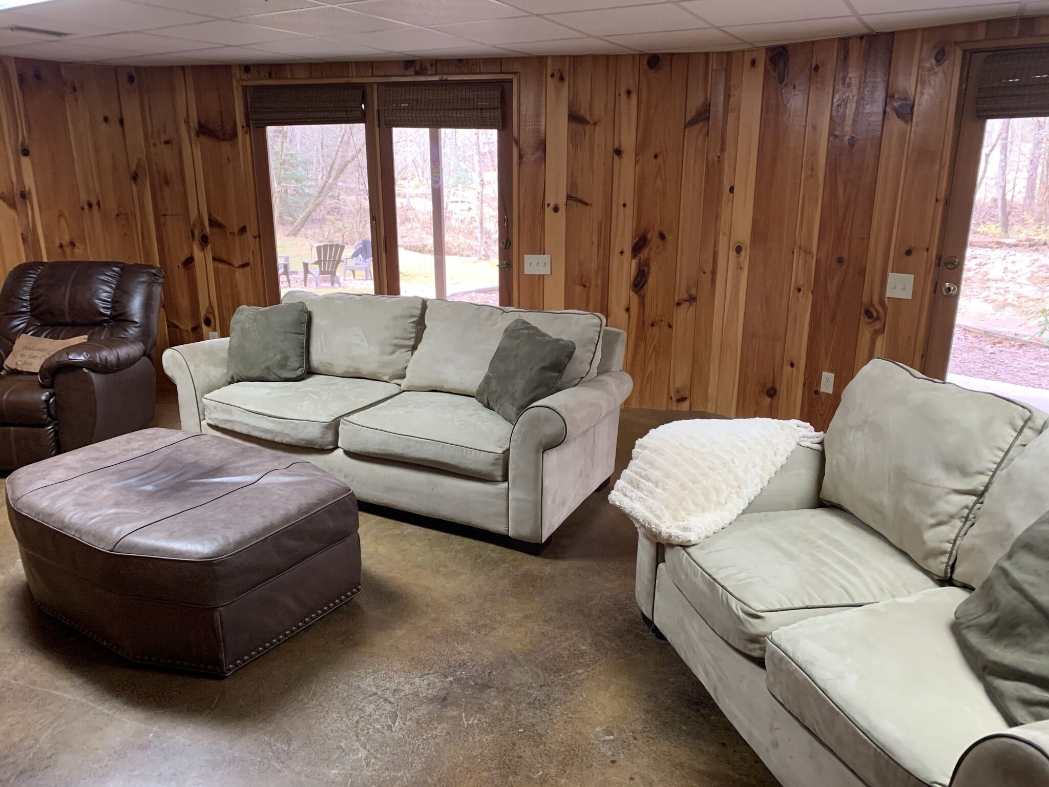 Ein gemütliches Wohnzimmer mit einer Eckcouch, einem Ledersessel und einem Hocker.