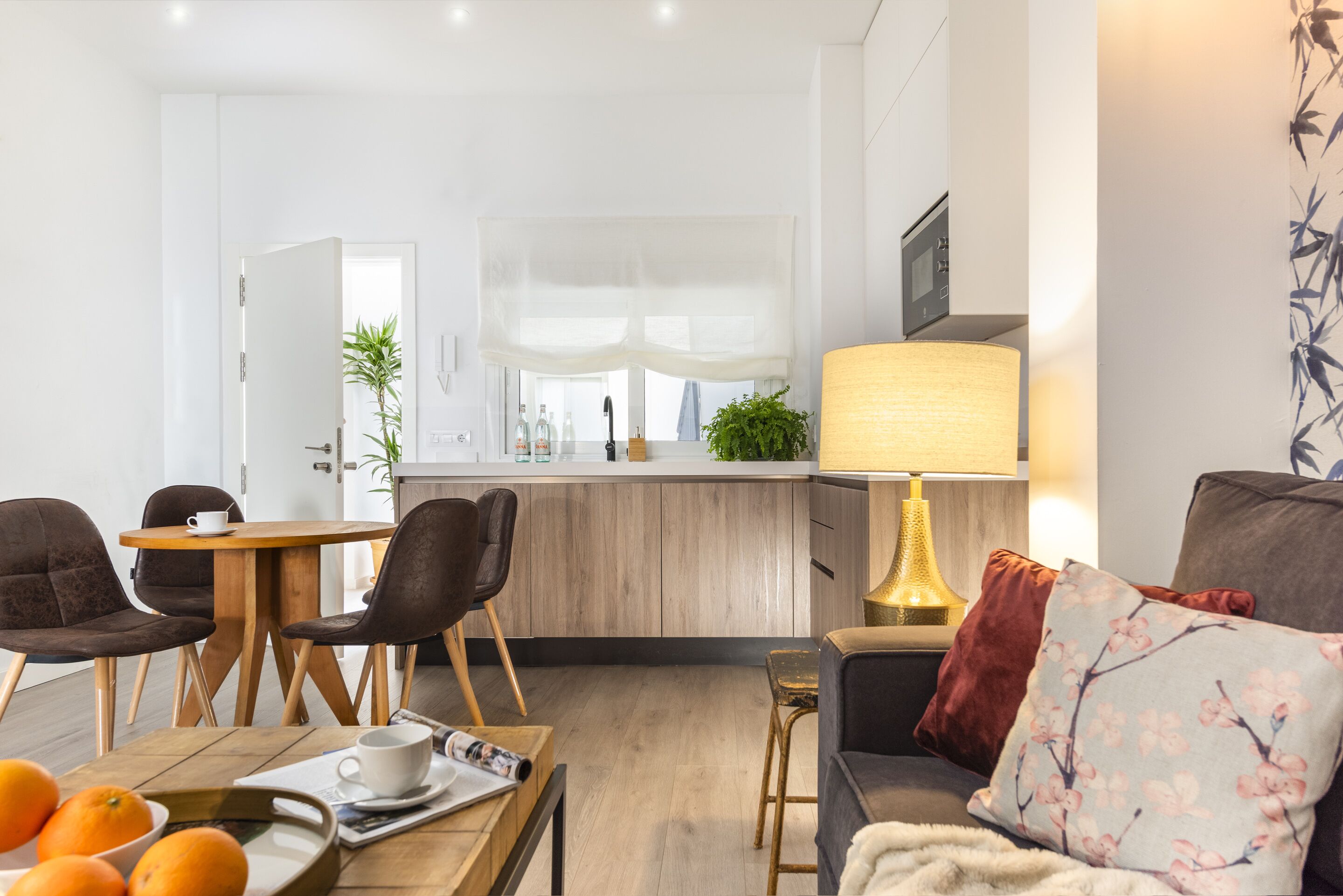 A modern living room with a sofa, a coffee table with oranges, and a dining area with chairs and a table.