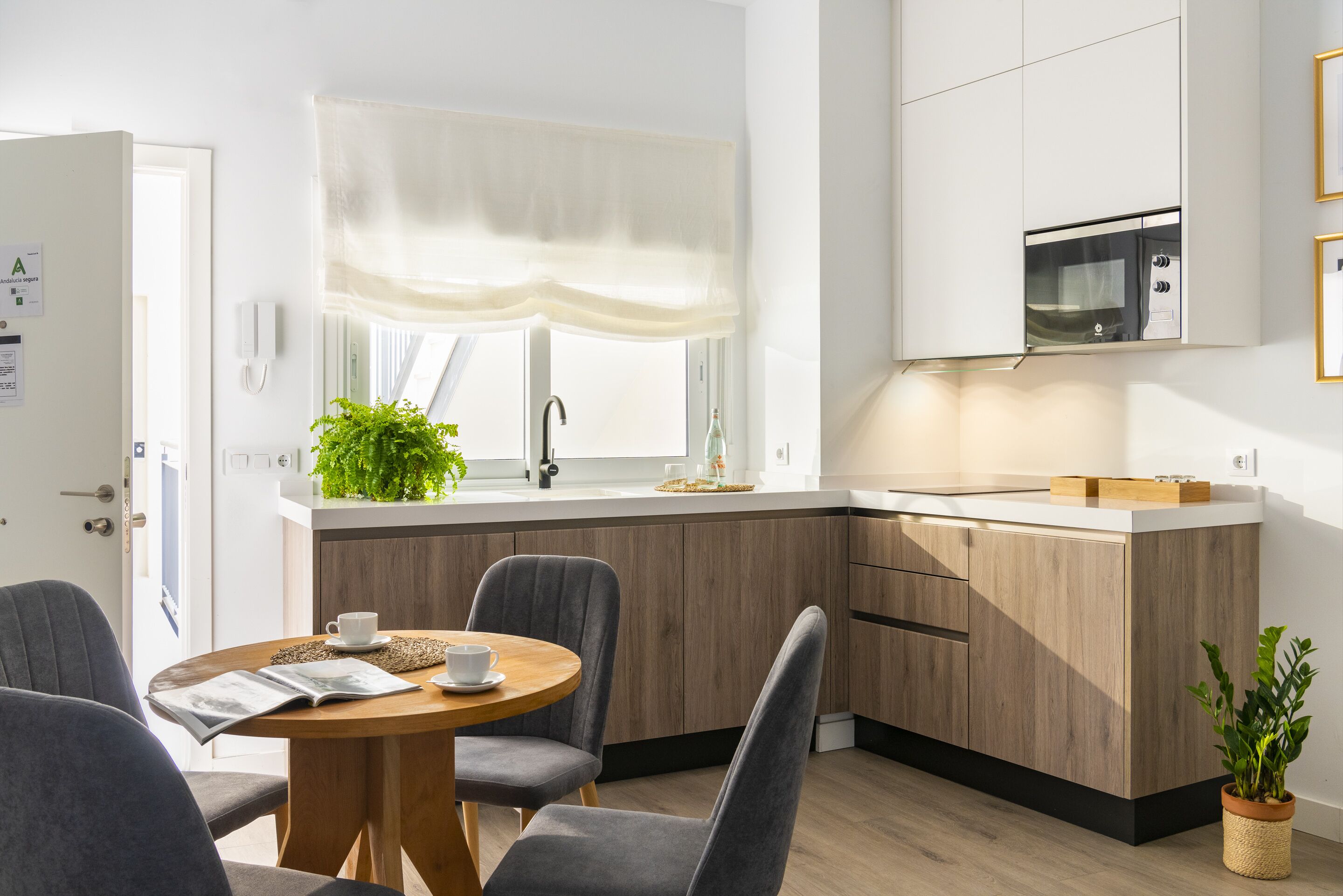 Eine moderne Küche mit einer Holz Arbeitsplatte, einer eingebauten Mikrowelle und einem Fenster mit transparenten Vorhängen.