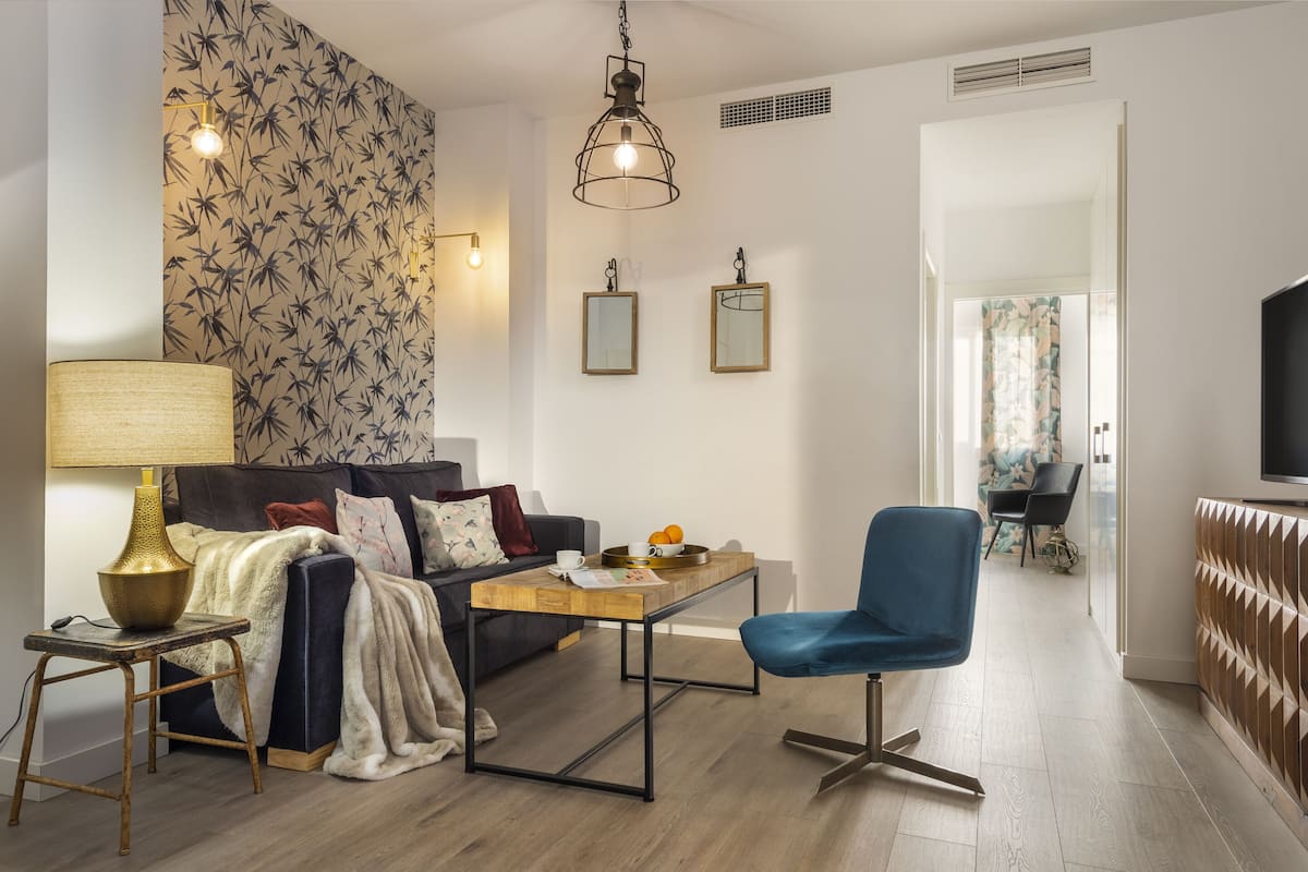 Un salon moderne avec un canapé, une table basse, un fauteuil bleu, une lampe et des appliques murales.