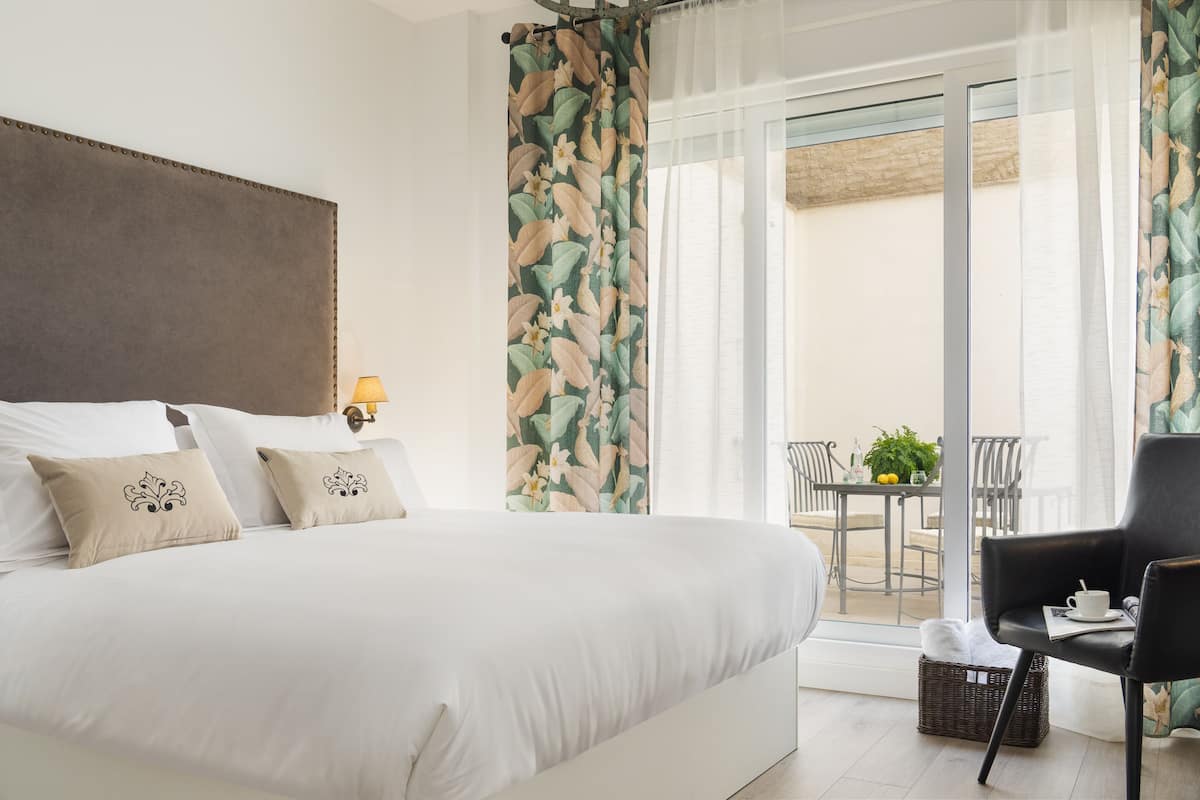 Une chambre avec un grand lit, une chaise, une table avec une plante, et un balcon avec une chaise et une table.
