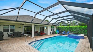 Ein überdachter Außenpool mit Terrasse, Liegestühlen und Grill.