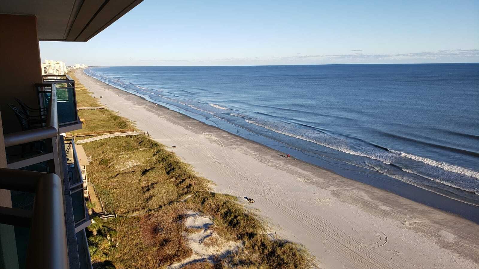 Une plage offrant une vue dégagée sur l’océan, un sentier de sable et des bâtiments en arrière-plan.