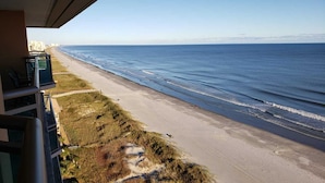 En strand med fri utsikt över havet, en sandstig och byggnader i bakgrunden.