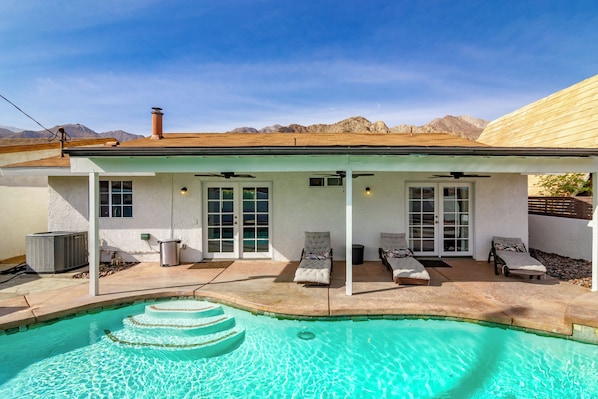 A house with a swimming pool, a covered patio with lounge chairs, and a mountain view.