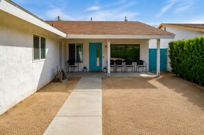 A covered patio area with a concrete pathway leading to a seating area with chairs and a table.