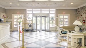 Un vestíbulo de hotel con una recepción, un área de espera con un sofá y sillones, una puerta giratoria y un piso con diseño.