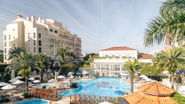 Un resort con una amplia piscina, palmeras y un edificio con balcones.