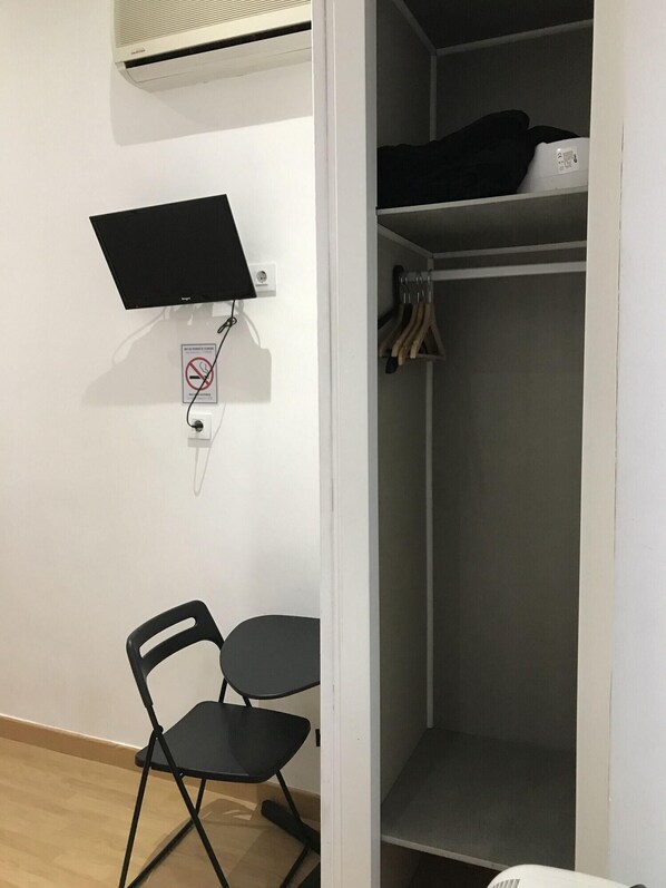 Ein Zimmer mit Schreibtisch, Stuhl und Kleiderschrank mit Kleidung.