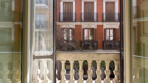 Blick durch ein Fenster eines Gebäudes mit Balkon, mit Ziegelaußenwand und mehreren Fenstern mit Fensterläden.