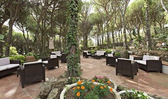 Un patio al aire libre con mobiliario de mimbre, suelo de piedra y diversas plantas y flores.