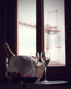 A table with a bottle of champagne, two wine glasses, a bowl of strawberries, and a white cloth.