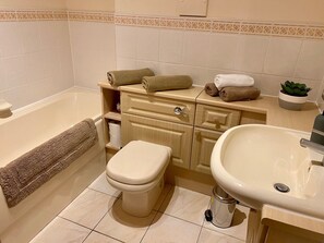 Een badkamer met toilet, wastafel en bad. Er liggen handdoeken op de wastafel en staat een plant op het aanrecht.