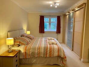 Een slaapkamer met een bed, twee bedlampen, een raam met gordijnen, een radiator en een schuifdeur met glas.