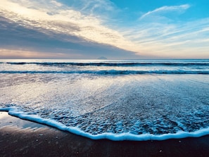 Uma praia com ondas suaves batendo na costa sob um céu parcialmente nublado.