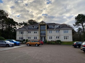 Een meerlaags woongebouw met een verharde oprit en verschillende geparkeerde auto's.