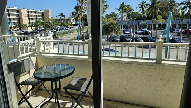 A balcony with a table and chairs, overlooking a parking area with cars and palm trees. - Exceptional Luxury Resort (Boynton Beach)