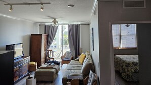 A living room with a sofa, a TV, a wooden cabinet, and a window with curtains. - Exceptional Luxury Resort (Boynton Beach)
