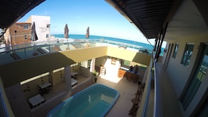 A pool area with a view of the ocean, outdoor seating, and a covered patio. - Pousada Porto Maraca (Ipojuca)